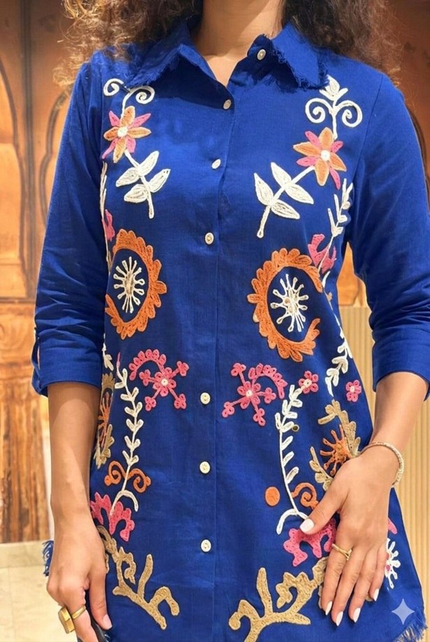 Close-up of multi-color floral embroidery and frayed collar on a cobalt blue linen shirt.