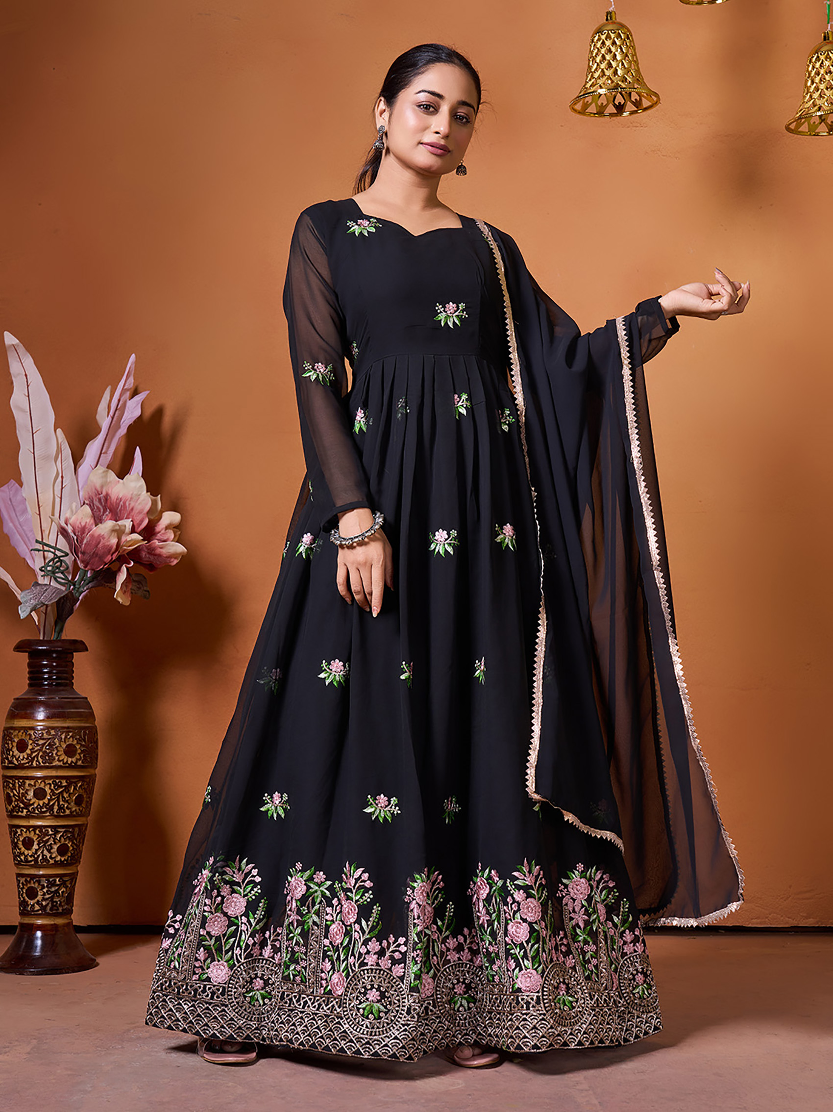 A woman wearing a floor-length black Anarkali gown with pink floral embroidery and a sheer dupatta.