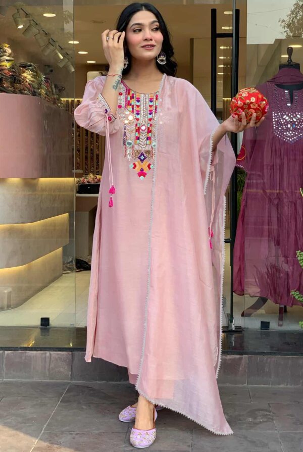 A woman wearing a light blush pink kaftan featuring a vibrant, multi-colored embroidered yoke with mirror work.