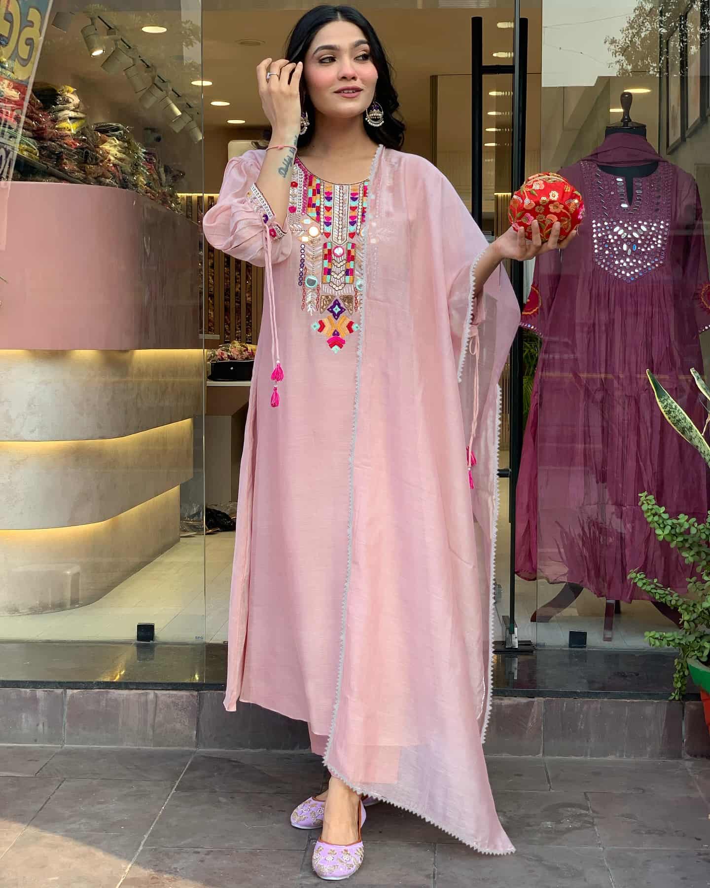 A woman wearing a light blush pink kaftan featuring a vibrant, multi-colored embroidered yoke with mirror work.