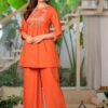 A woman posing in a deep burnt orange flared silk Anarkali featuring silver neckline embroidery and a matching dupatta.