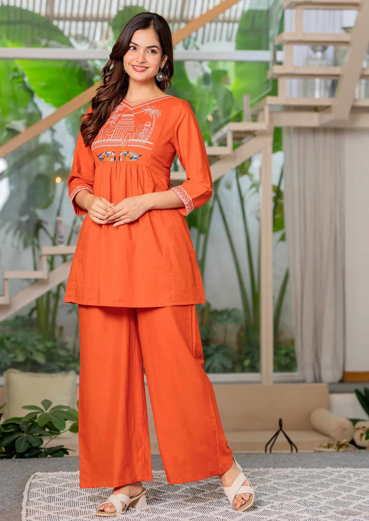 A woman posing in a deep burnt orange flared silk Anarkali featuring silver neckline embroidery and a matching dupatta.