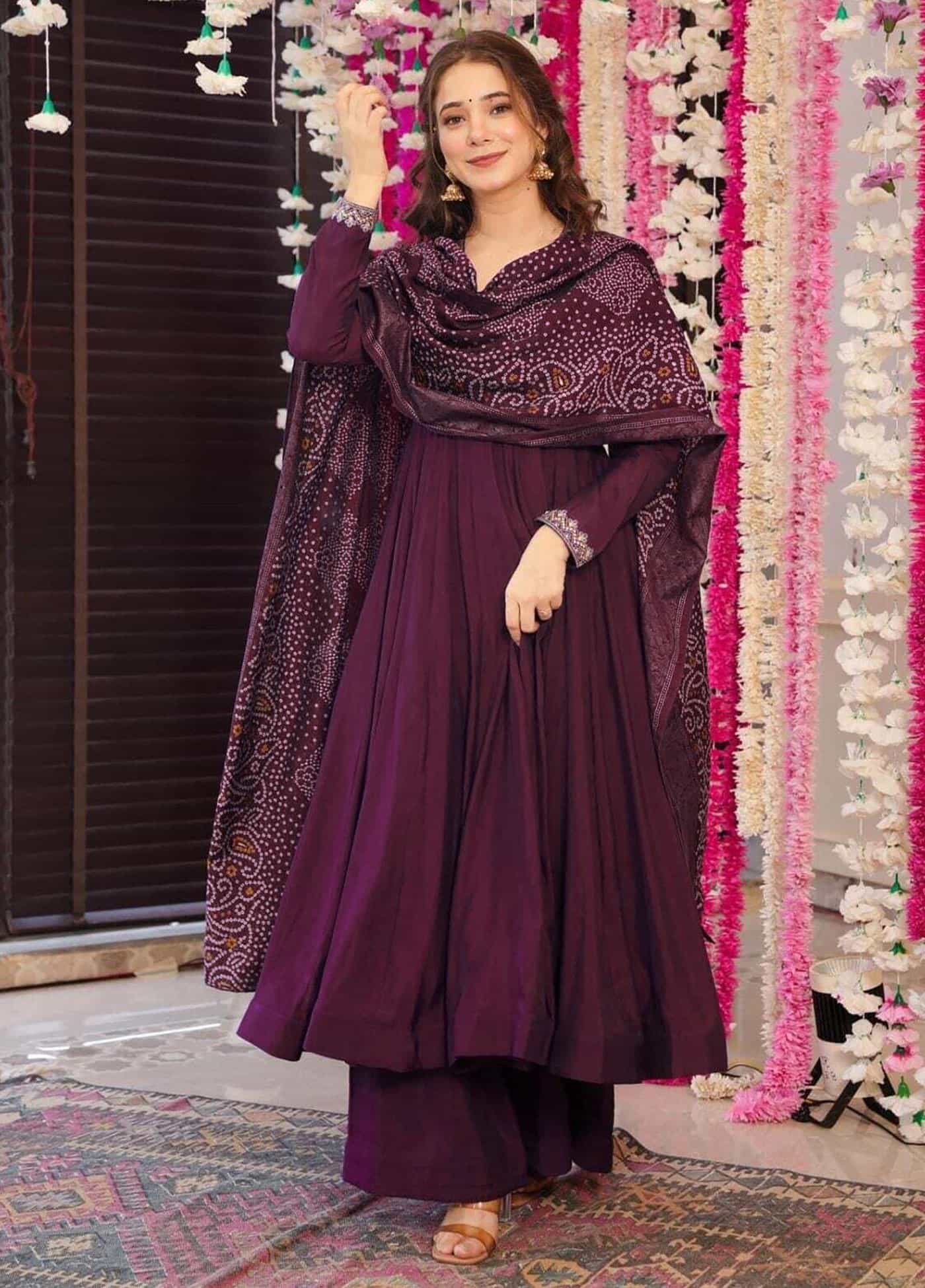 A woman wearing a deep wine-colored flared Anarkali kurta with silver neckline embroidery and a matching Bandhani print dupatta.
