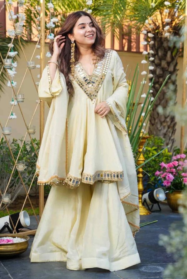 A woman in an ivory organza peplum kurta featuring a heavy mirror-work V-neckline and matching flared sharara pants.