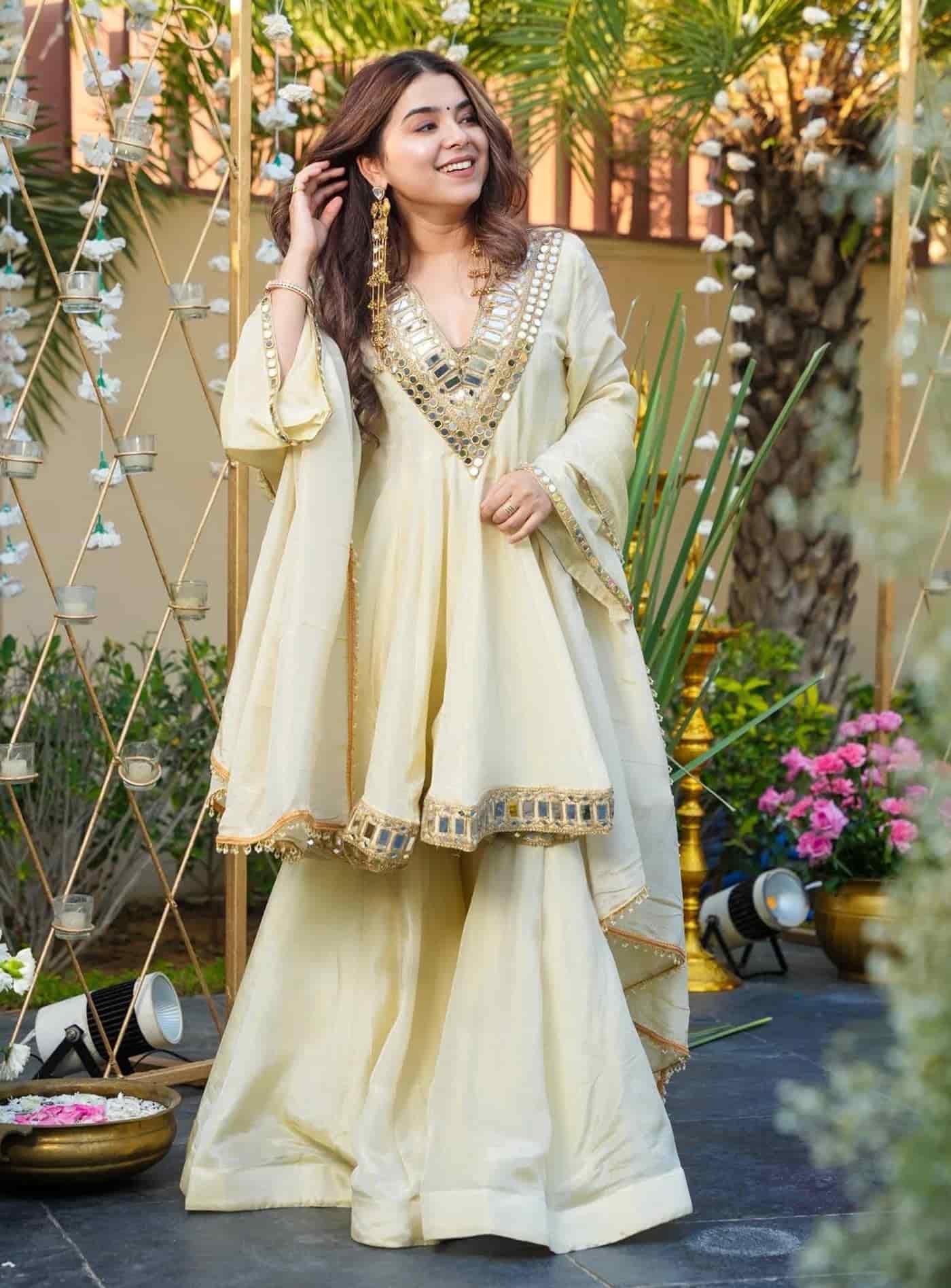A woman in an ivory organza peplum kurta featuring a heavy mirror-work V-neckline and matching flared sharara pants.
