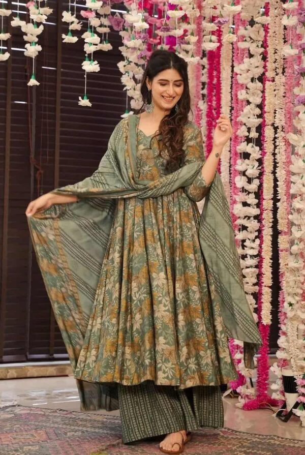 A woman posing in a flared olive green Anarkali featuring earth-toned floral prints and a matching dupatta with striped palazzo pants.