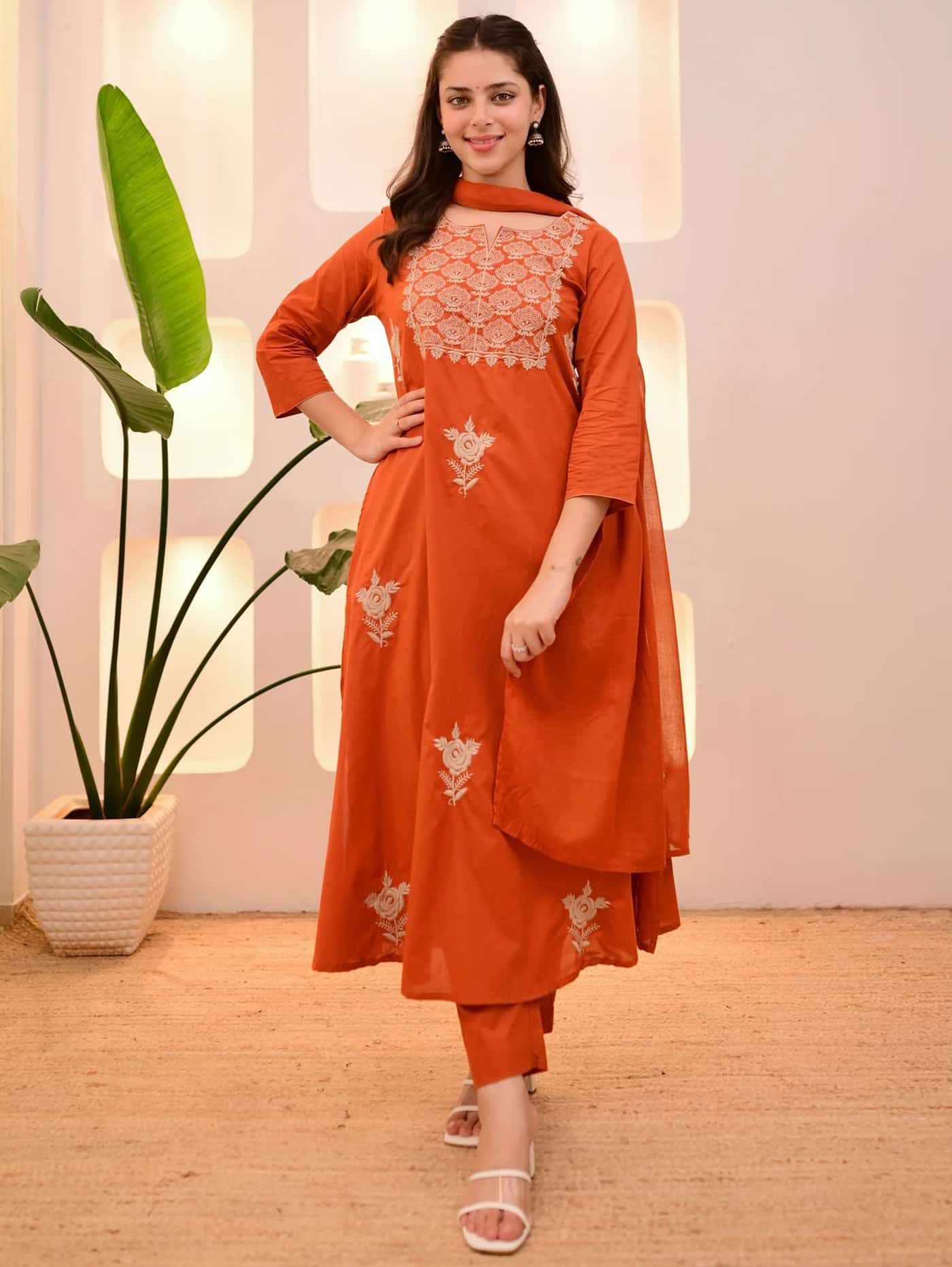 A woman in a burnt orange A-line silk kurta featuring ivory floral embroidery on the yoke and matching straight-fit pants.