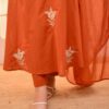 A close-up of the lower half of the saffron orange silk set, showing the straight-fit trousers and the delicate floral embroidery on the kurta’s hem.