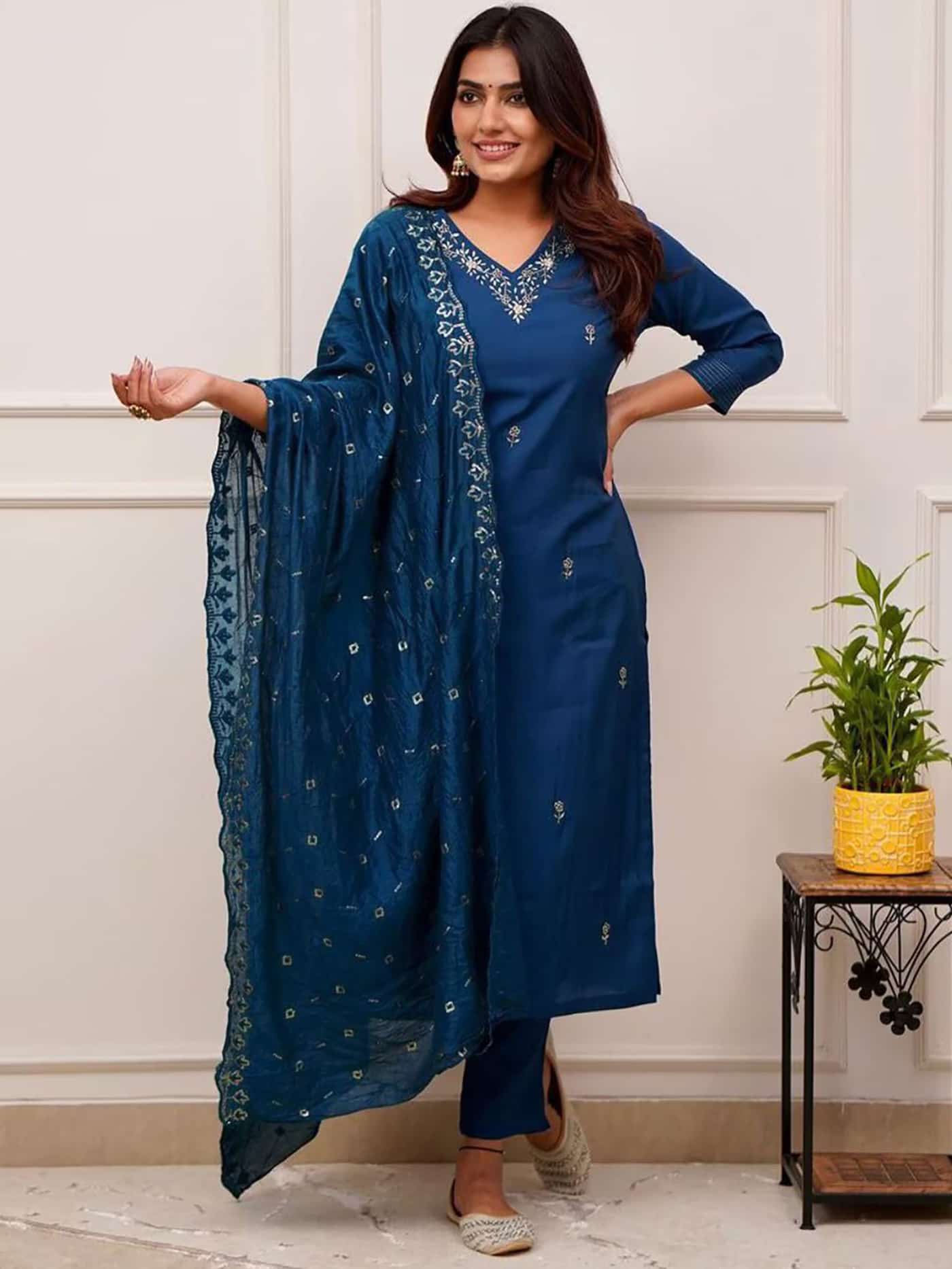 A woman in a deep sapphire blue straight-fit silk kurta featuring a silver embroidered V-neckline and matching pants.