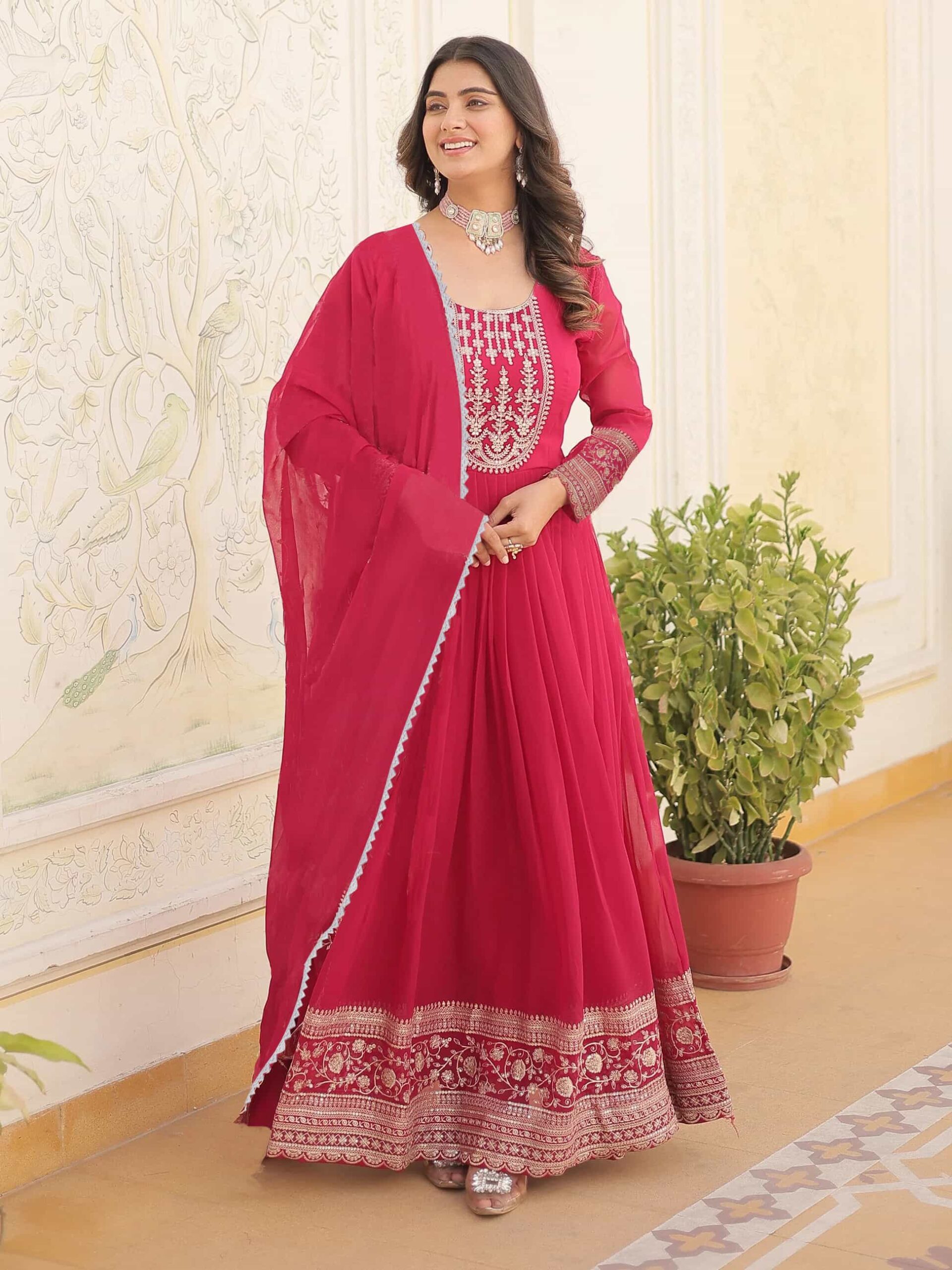 A woman in a premium scarlet red Anarkali gown with intricate silver zari embroidery on the bodice.