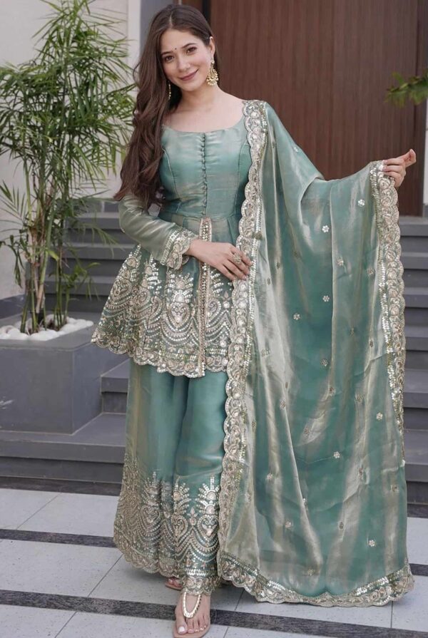 A woman in a seafoam green silk peplum kurta featuring heavy gold embroidery and matching flared sharara pants.