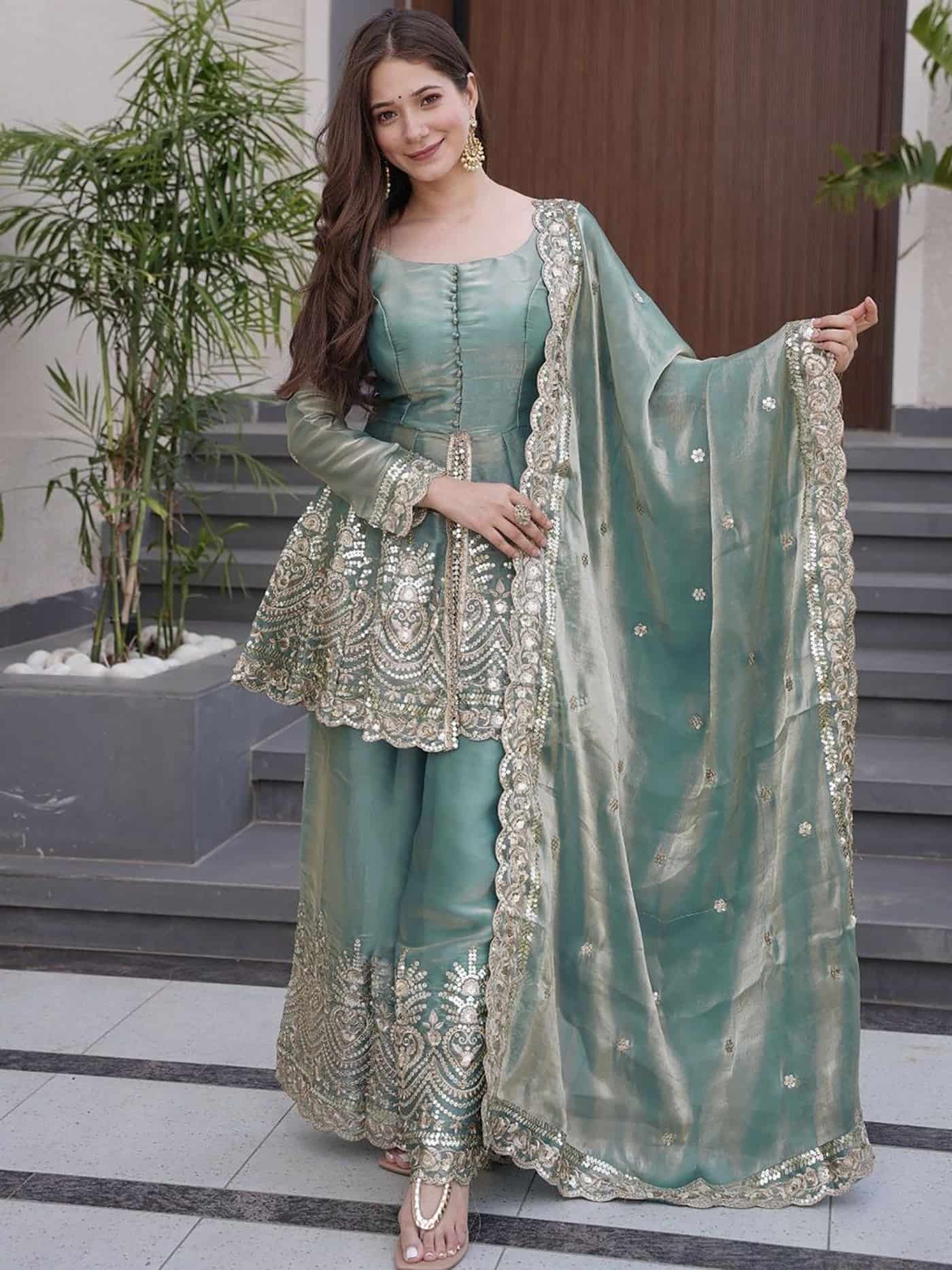 A woman in a seafoam green silk peplum kurta featuring heavy gold embroidery and matching flared sharara pants.