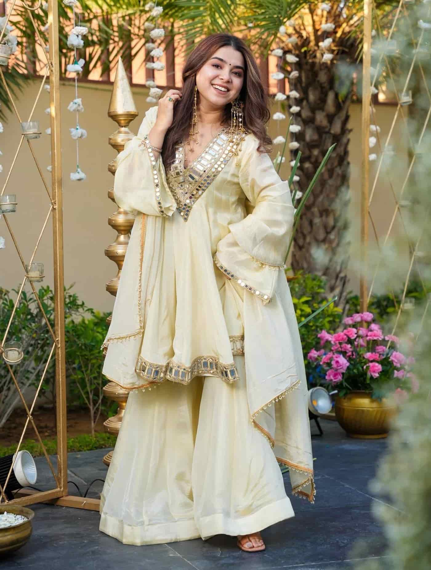 Side profile of an ivory peplum suit highlighting the mirror-trimmed bell sleeves and wide-leg sharara pants.