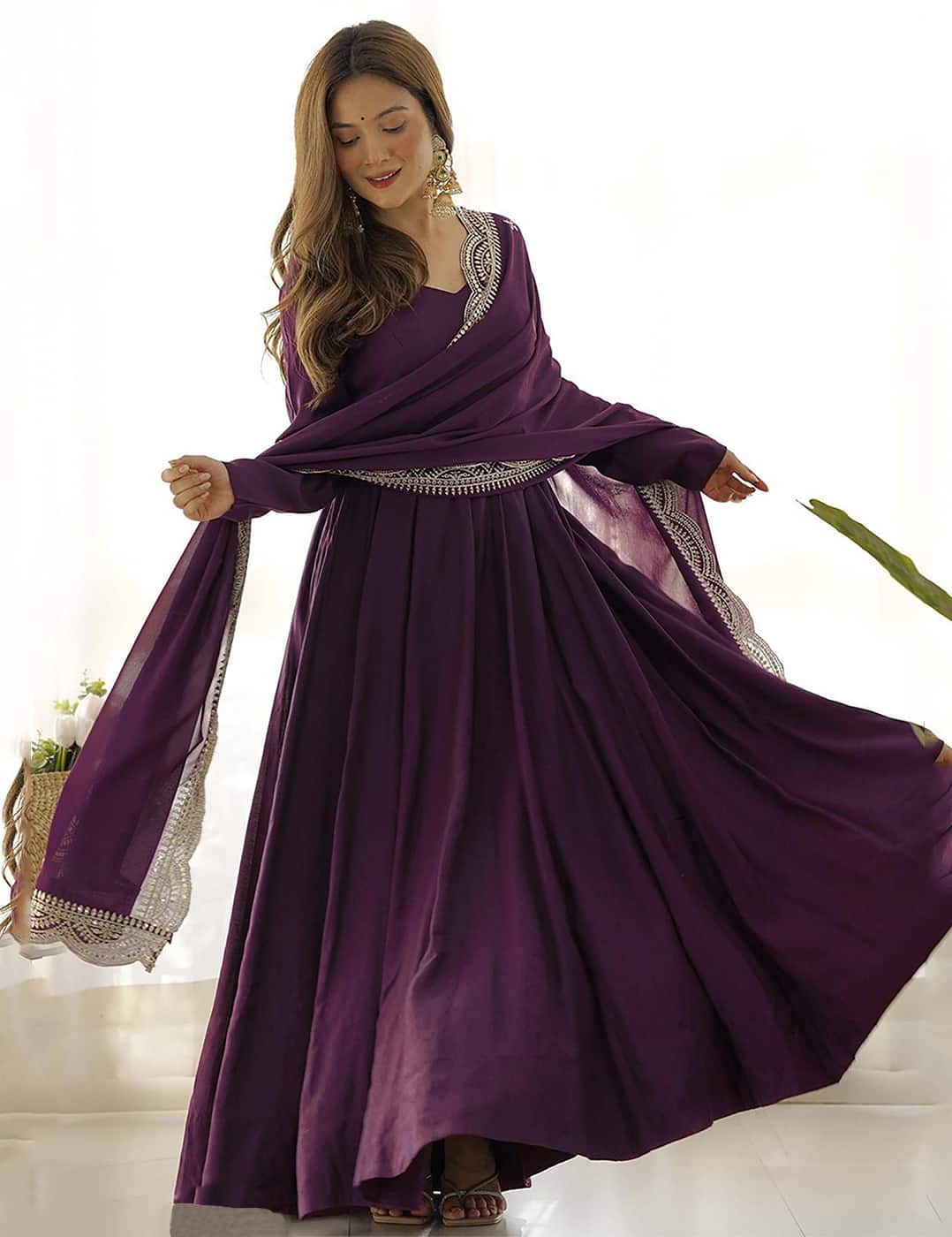 A model wearing a wine purple embroidered suit set in a bright, minimalist room, showcasing the drape and movement of the fabric.